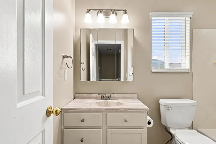 Single vanity with an integrated sink, medicine cabinet with mirrored doors, vanity light fixture, and a toilet