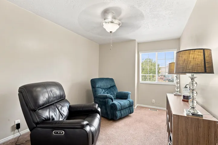 Carpeted flooring, neutral wall paint, ceiling fan light fixture, and a window providing natural light