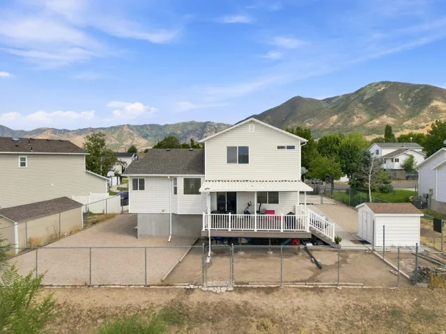 Two-story property with white siding, an expansive elevated deck, and a chain-link fenced yard with a storage shed