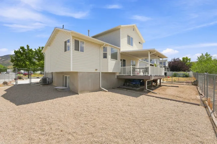 Exterior featuring light-toned siding, a covered deck with white railing, and a gravel-paved area