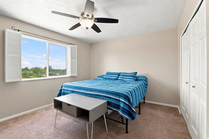 Carpeted flooring with painted walls, a ceiling fan with integrated lighting, and a window with louvered shutters