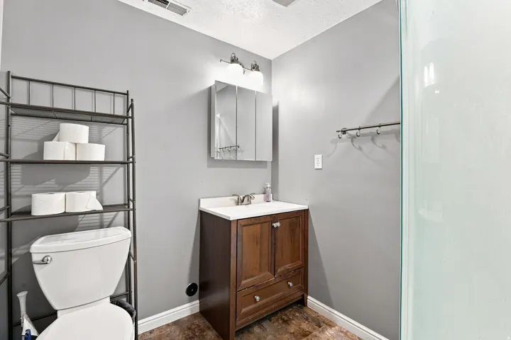 Wood-finish flooring, wood vanity with white countertop, chrome faucet, mirrored medicine cabinet, and glass-enclosed shower