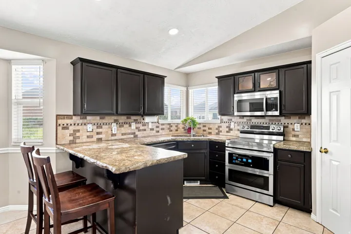 U-shaped kitchen featuring dark wood cabinetry, stainless steel appliances, a tile backsplash, and a breakfast bar