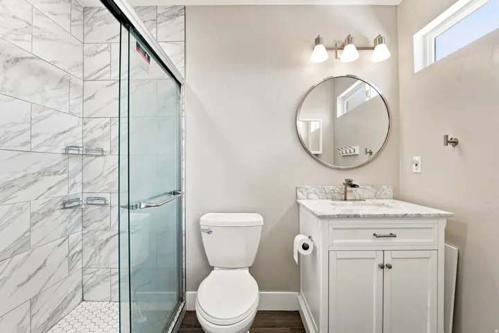 Glass-enclosed shower with white marble-look subway tile and hexagonal floor tile