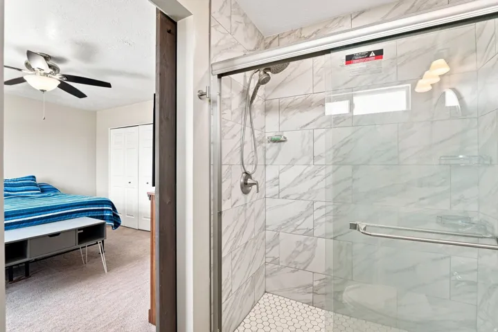Enclosed shower with full-height tile surround, hexagon tile flooring, and sliding glass door
