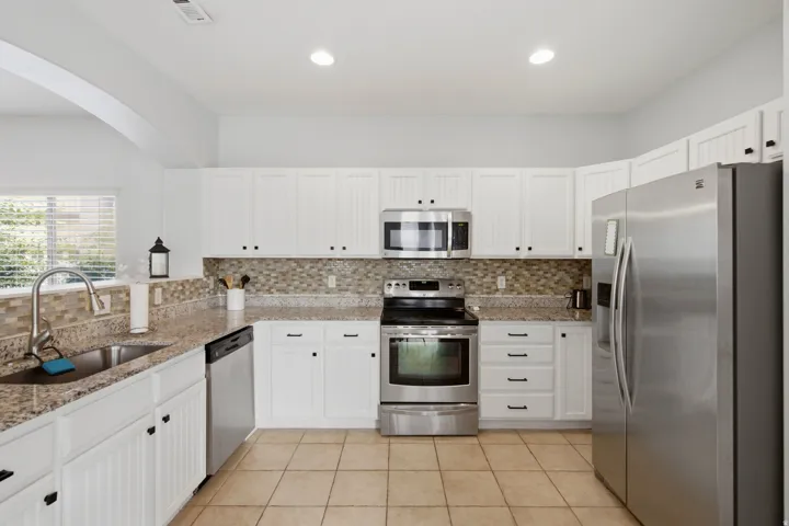 White cabinetry with black hardware, mosaic tile backsplash, stainless steel appliances, granite countertops, and tile flooring