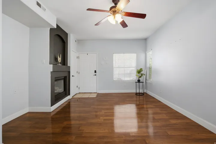Wood-finish flooring, built-in fireplace with alcove, ceiling fan, and multiple windows with blinds