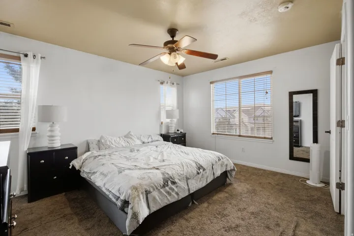 Carpeted bedroom featuring a ceiling fan, two windows with blinds, and white wall finishes