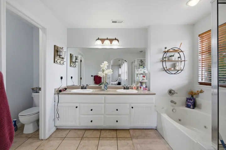 Dual vanity with white cabinetry, a large integrated mirror, and overhead lighting