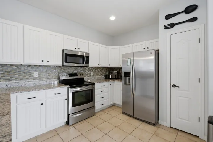 White shaker-style cabinetry with black hardware, mosaic tile backsplash, stainless steel appliances, and light-toned countertops