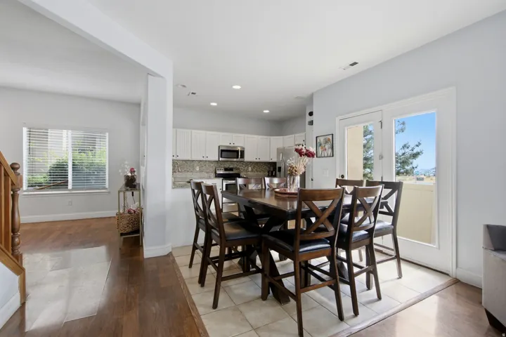 Open-concept dining and kitchen area featuring a round wood dining table with seating for six, white cabinetry, stainless steel appliances, tile flooring, recessed lighting, and glass sliding doors opening to outdoor space with natural light throughout