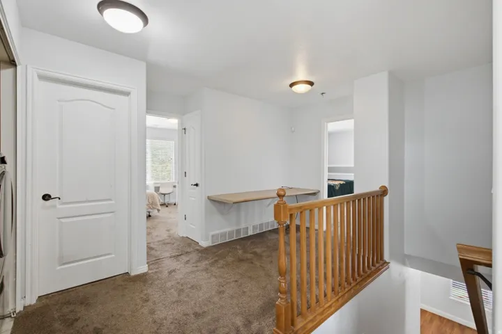 Carpeted hallway with a built-in desk, wood baluster railing, and ceiling-mounted lighting fixtures