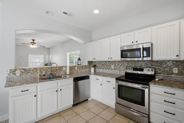 White cabinetry with beadboard paneling, stainless steel appliances, speckled countertops, and a mosaic tile backsplash