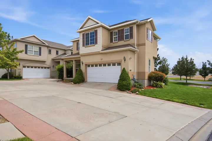 Stucco exterior featuring multiple garages, a covered entry, and established landscaping
