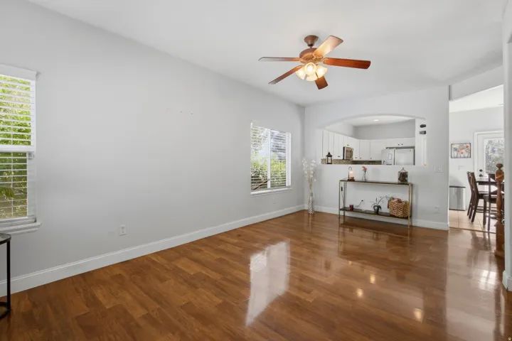 Wood-finish flooring, ceiling fan, multiple windows with blinds, arched pass-through, and built-in white cabinetry