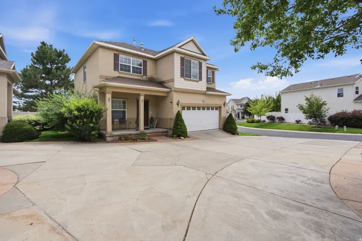 Two-story residence featuring a covered front porch, attached garage, and mature landscaping