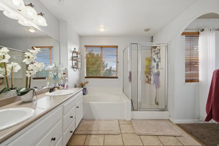Double vanity with integrated sinks, a large mirror, a built-in soaking tub, a glass-enclosed shower, and tiled flooring