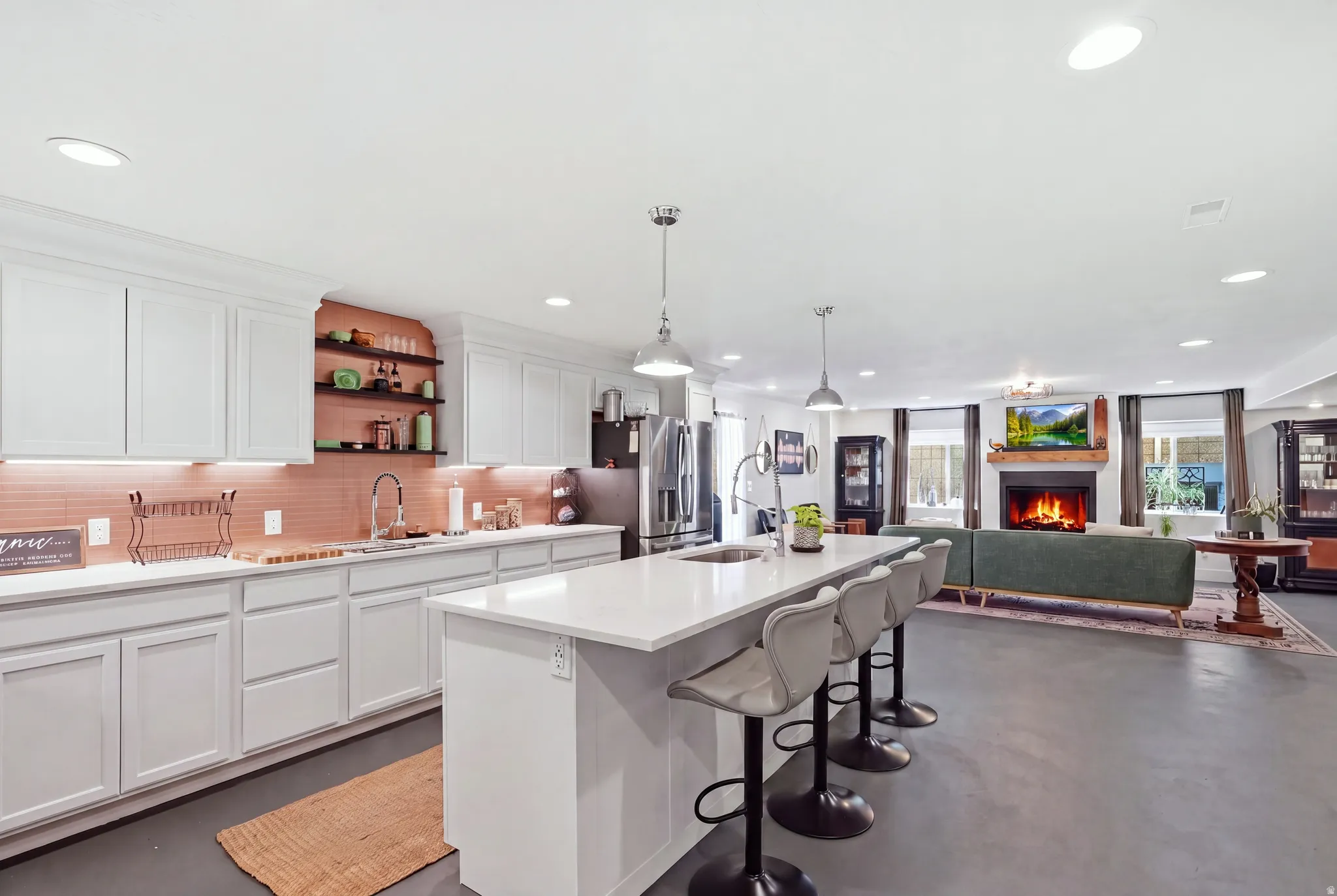 Open-concept interior featuring a kitchen island with seating, white cabinetry, and a fireplace with a wood mantel
