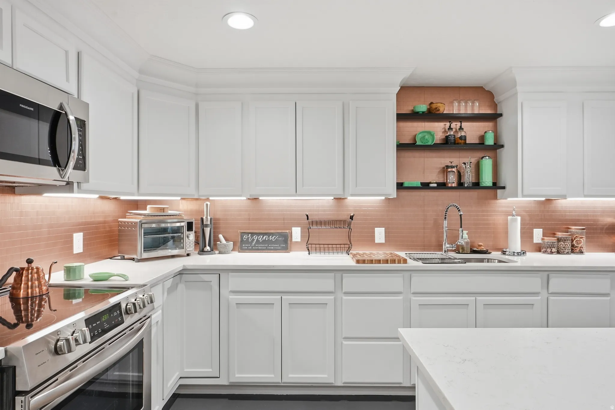 White cabinetry with crown molding, stainless steel appliances, recessed lighting, under-cabinet lighting, and a copper-toned tile backsplash