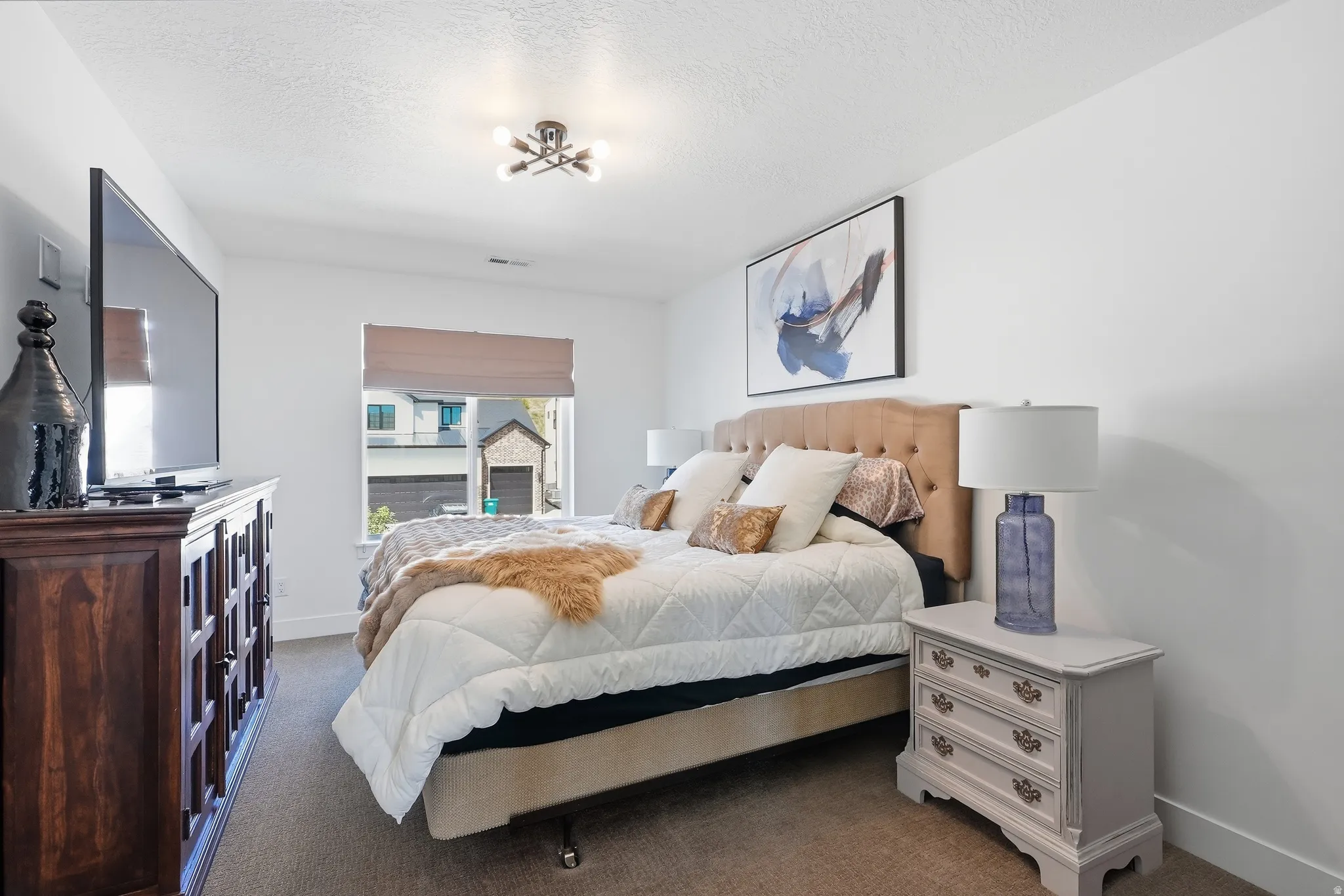 Recessed window with shade, plush carpeting, ceiling-mounted light fixture, light-colored walls, and a wooden credenza