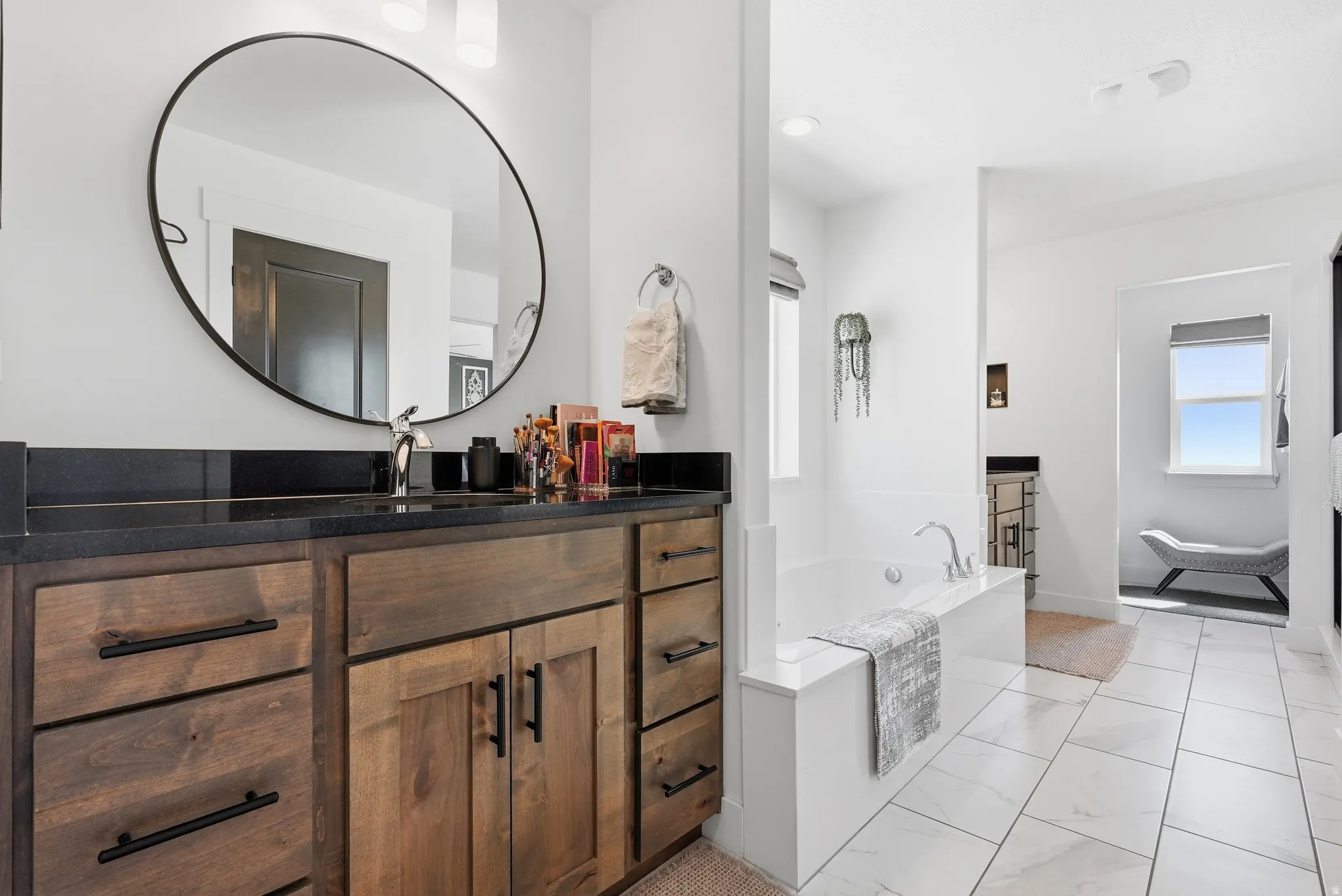 White tiled flooring, built-in bathtub, and a dark wood-finish vanity with a dark countertop