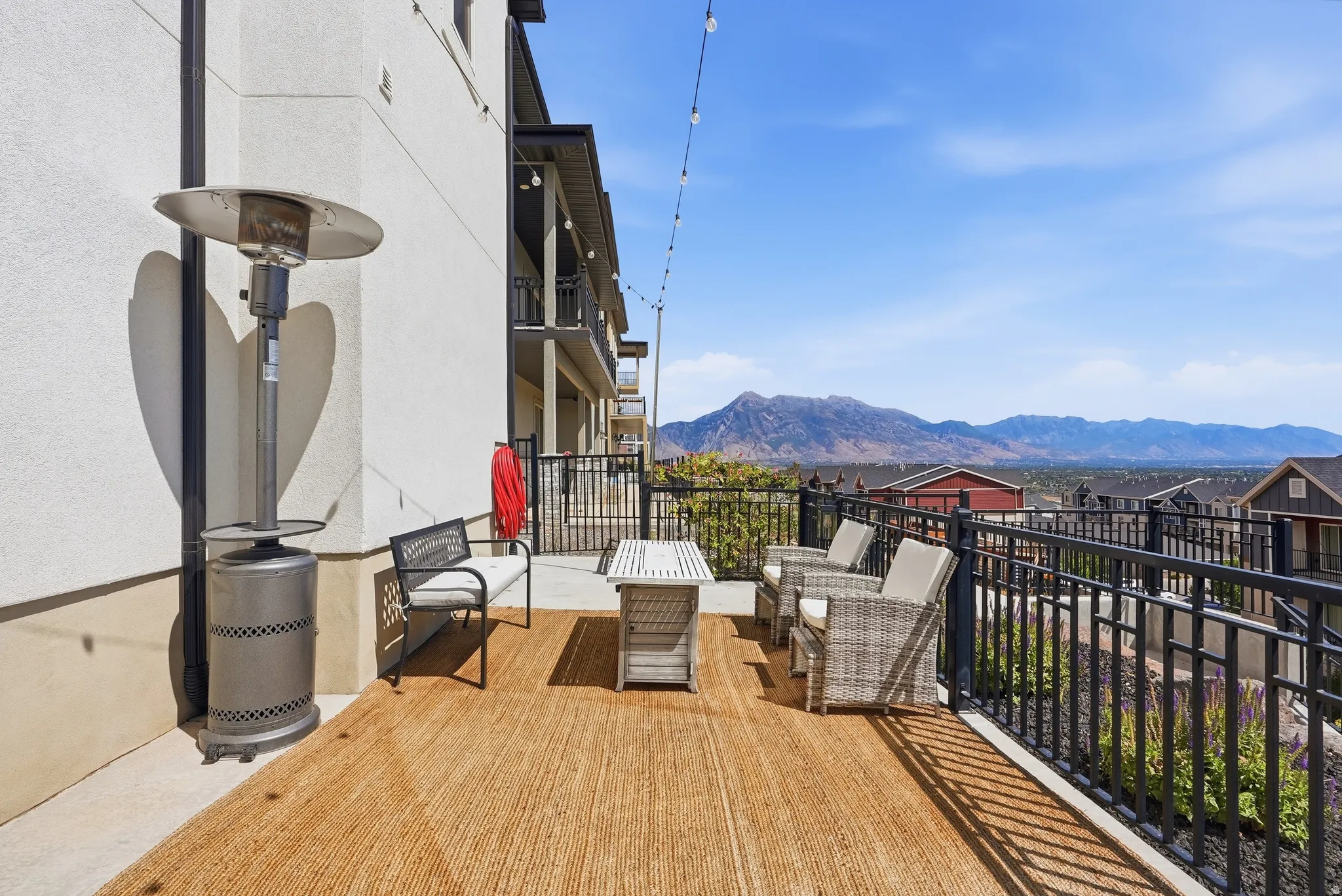 Expansive outdoor patio with a mountain backdrop, featuring a black metal railing and string lighting