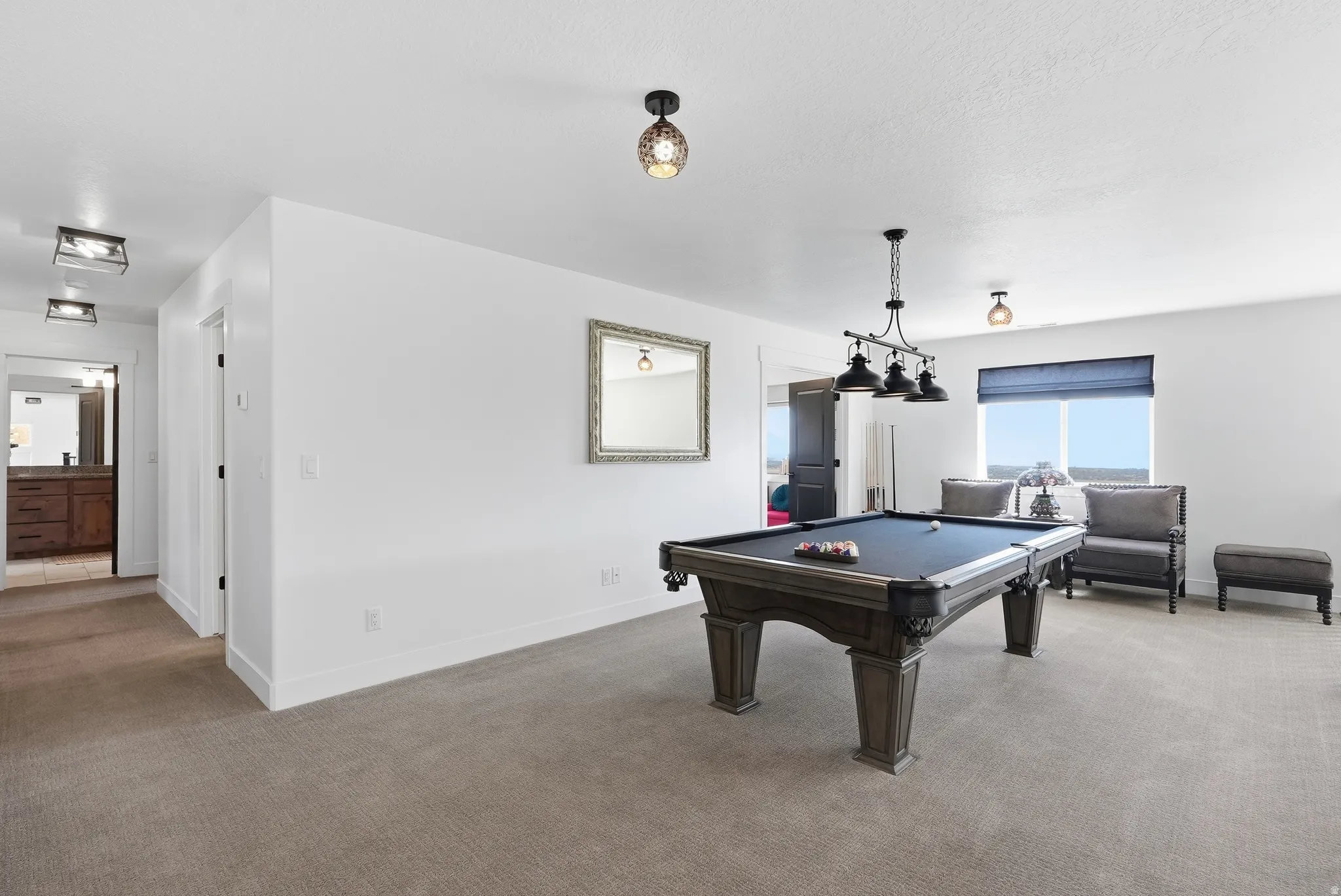 Spacious recreation room featuring a billiards table with a multi-light fixture, carpeted flooring, and ample natural light from a large window