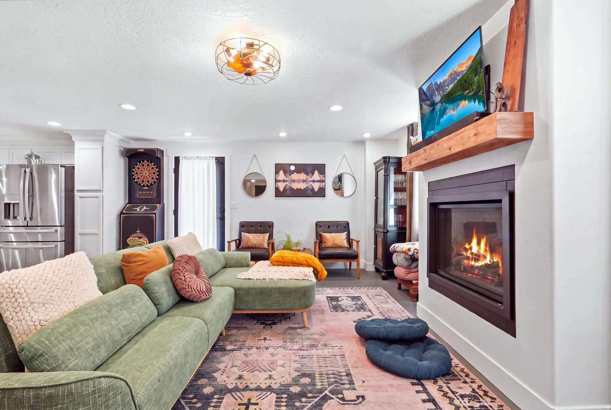 Built-in fireplace with a wood-finish mantel, stainless steel refrigerator, white cabinetry, and recessed lighting
