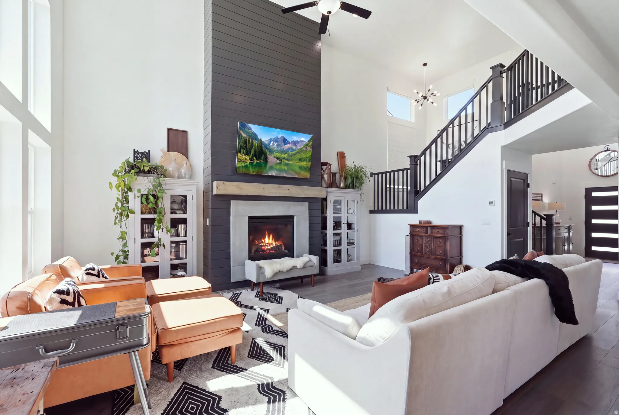 Soaring two-story living space anchored by a gas fireplace with surround cabinetry and shelving, hardwood flooring throughout, and abundant natural light from expansive windows
