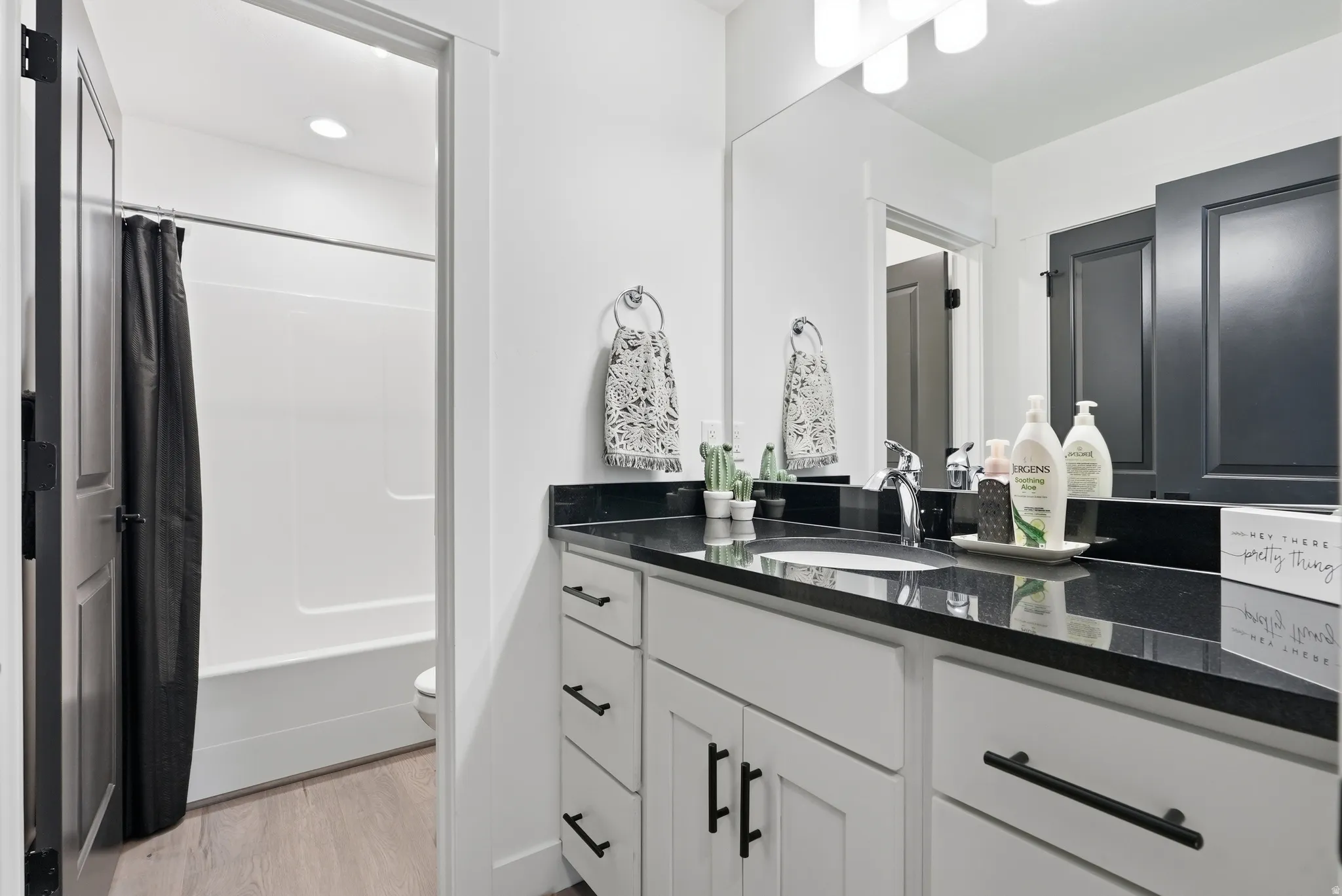 Bathroom featuring a vanity with white cabinetry, dark countertop, single basin sink, and a built-in mirror