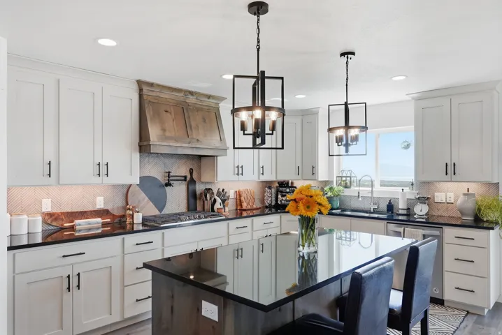 Kitchen featuring white cabinetry, dark countertops, a wood-finish range hood, an island with seating, and pendant lighting