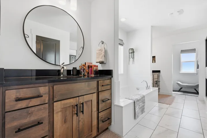 White tiled flooring, built-in bathtub, and a dark wood-finish vanity with a dark countertop