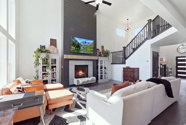 Soaring two-story living space anchored by a gas fireplace with surround cabinetry and shelving, hardwood flooring throughout, and abundant natural light from expansive windows