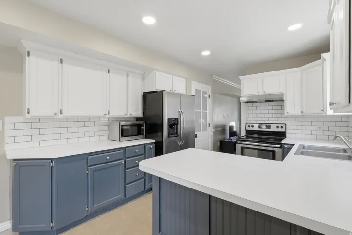 Kitchen featuring white upper cabinetry, blue lower cabinetry, white countertops, a white subway tile backsplash, and stainless steel appliances