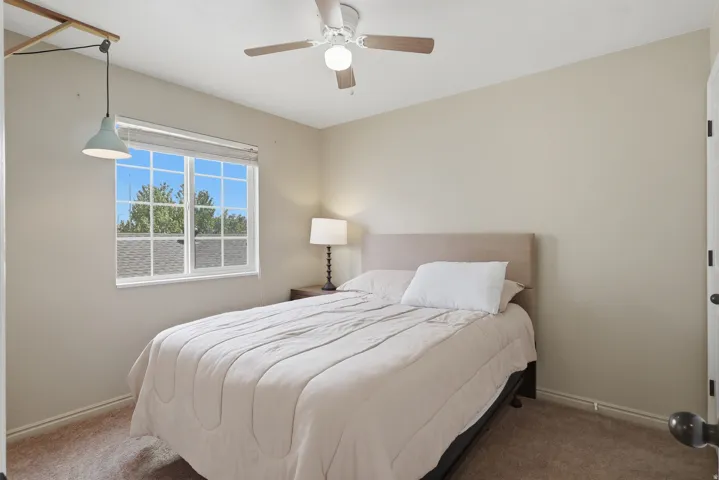 Ceiling fan, window with grid pattern, wall-mounted light fixture, neutral wall color, and carpeted flooring