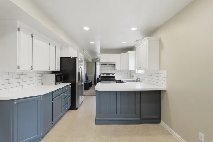 Bright kitchen featuring white upper cabinetry, blue lower cabinetry, white countertops, and subway tile backsplash