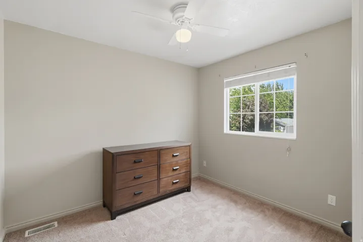 Carpeted flooring, neutral wall color, white ceiling fan, and a window with white trim