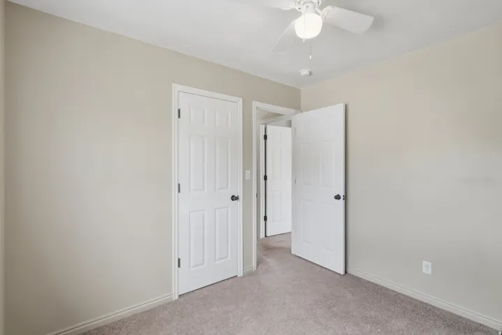 Neutral-toned walls with ceiling fan and carpeted flooring