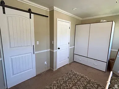 Crown molding, two-tone wall treatment, barn door with black hardware, and an additional white door with black knob