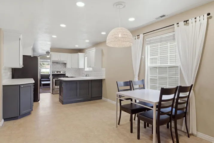 Kitchen featuring white subway tile backsplash, white upper cabinetry, and dark lower cabinetry with light countertops