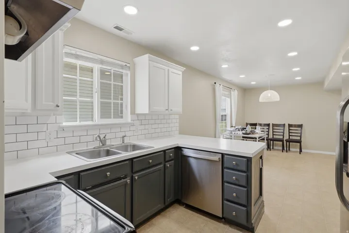 Kitchen featuring white subway tile backsplash, white countertops, two-tone cabinetry, stainless steel dishwasher, and recessed lighting