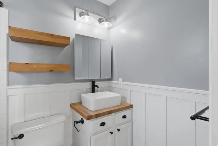 White shaker-style vanity with a wood-finish countertop, rectangular vessel sink, and matte black faucet