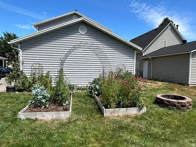 Siding exterior, two raised garden beds, and a brick-built fire pit