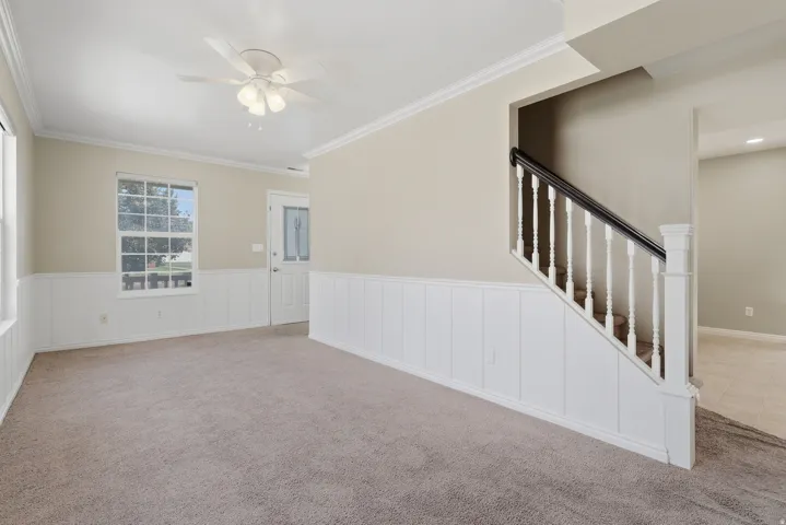 Spacious great room featuring neutral wall finishes with decorative wainscoting, plush carpet flooring, and a ceiling fan with integrated lighting