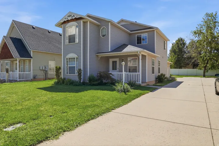 Two-story exterior with light gray siding, a covered entry porch with white railings, and a paved driveway leading to the rear