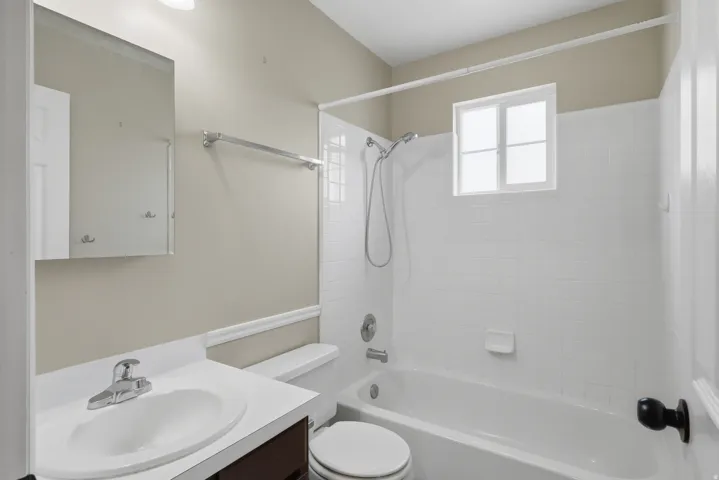 Bathroom featuring a white bathtub, ceramic tile shower surround, window with grid panes, vanity with an integrated sink, and a wall-mounted mirror
