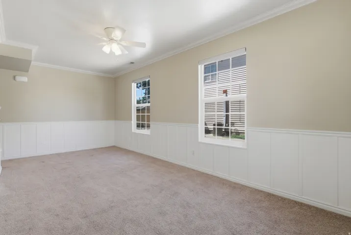 Carpeted room featuring two windows, wainscoting, crown molding, and a ceiling fan