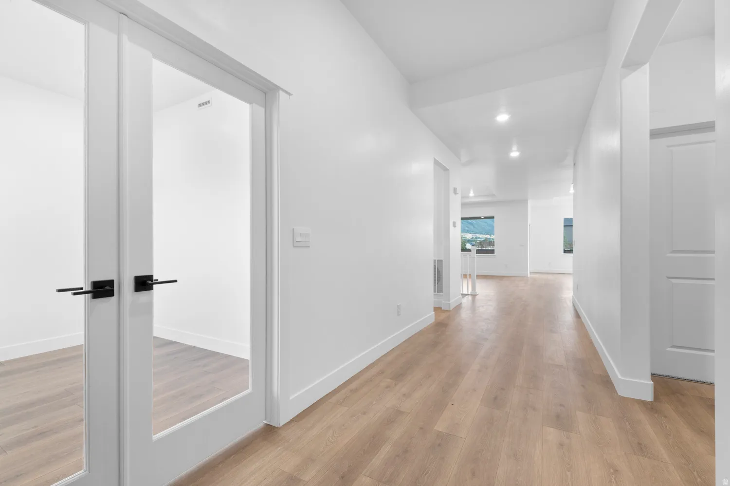 Light wood-finish flooring extending throughout, contemporary white walls, and recessed lighting