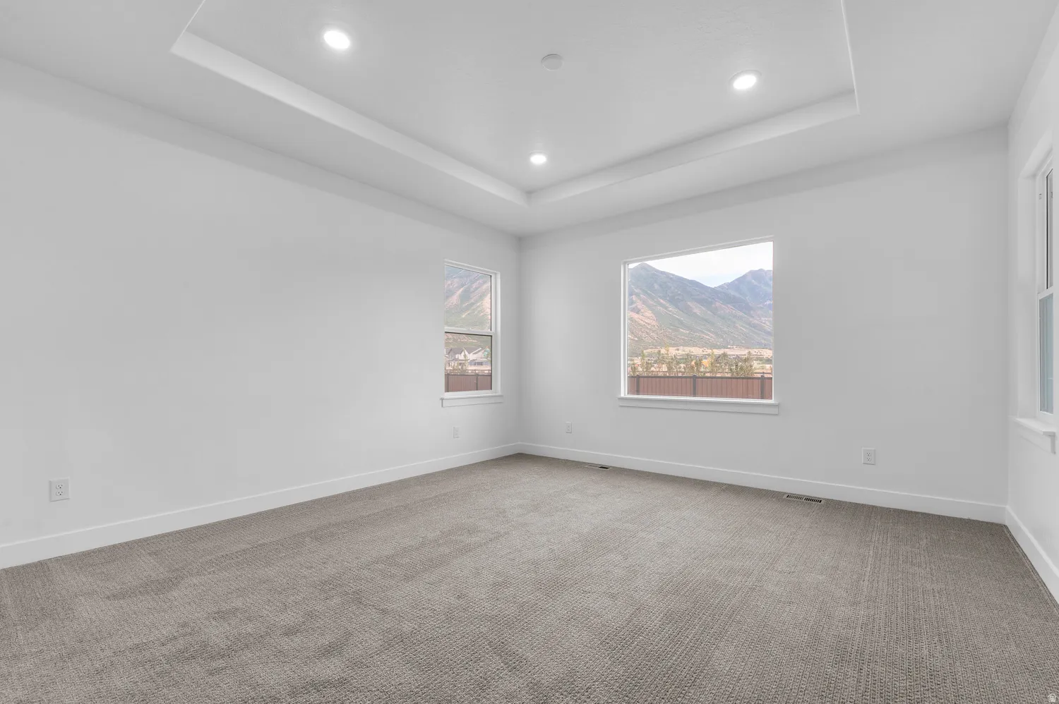 Tray ceiling with recessed lighting, neutral tone carpeting, white walls, and multiple windows