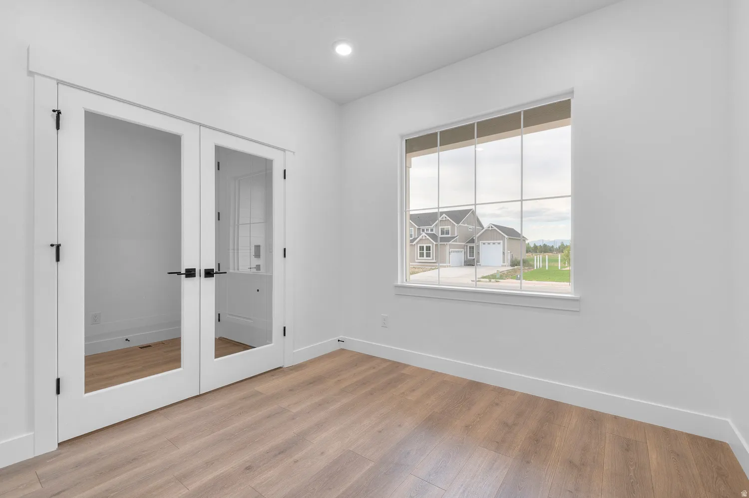 Wood-finish flooring, white walls, recessed ceiling lighting, and a large window with grid panes
